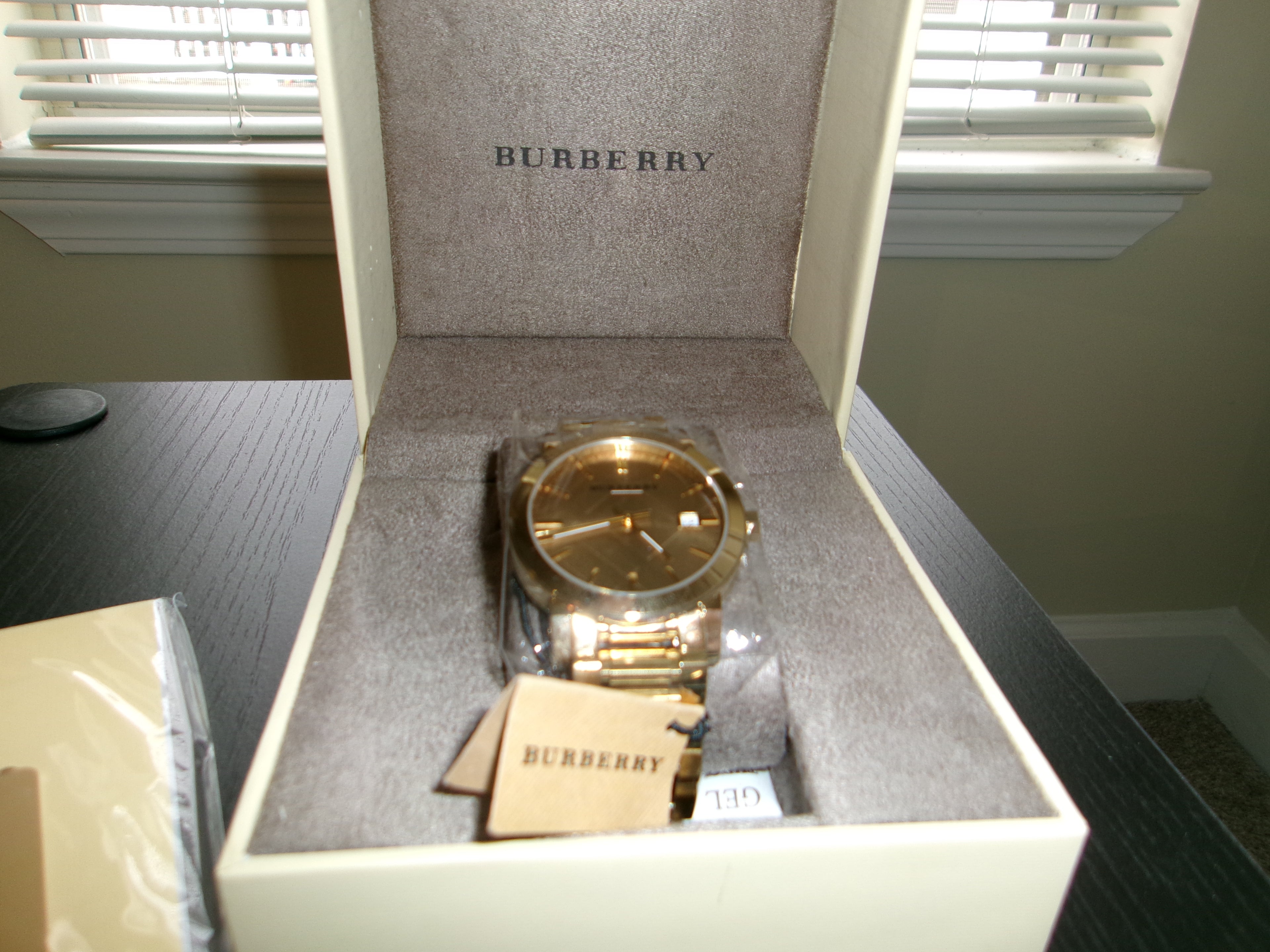 Gold Burberry watch in an open Burberry box on a table.