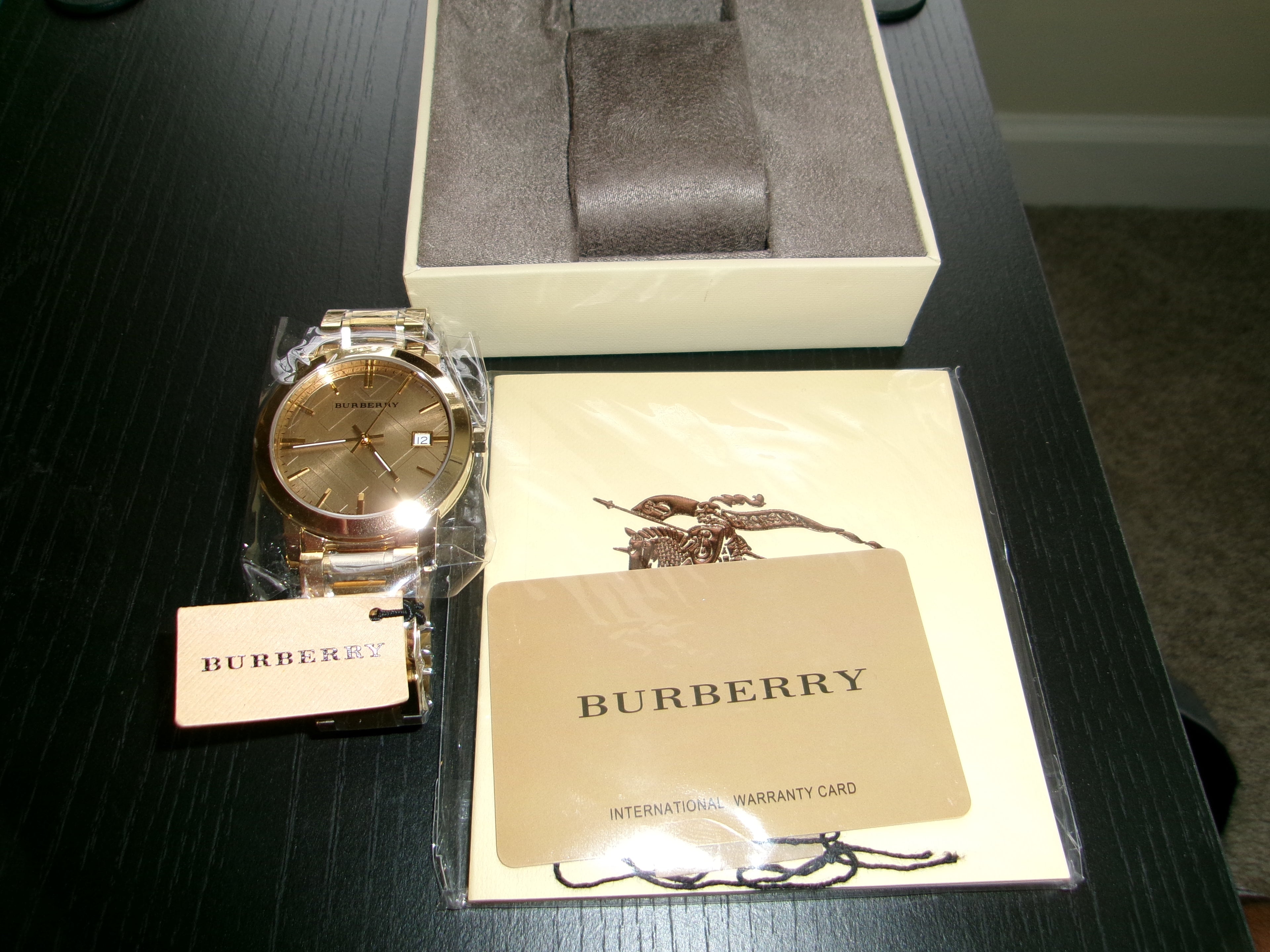 Gold Burberry watch with packaging and warranty card on a dark surface