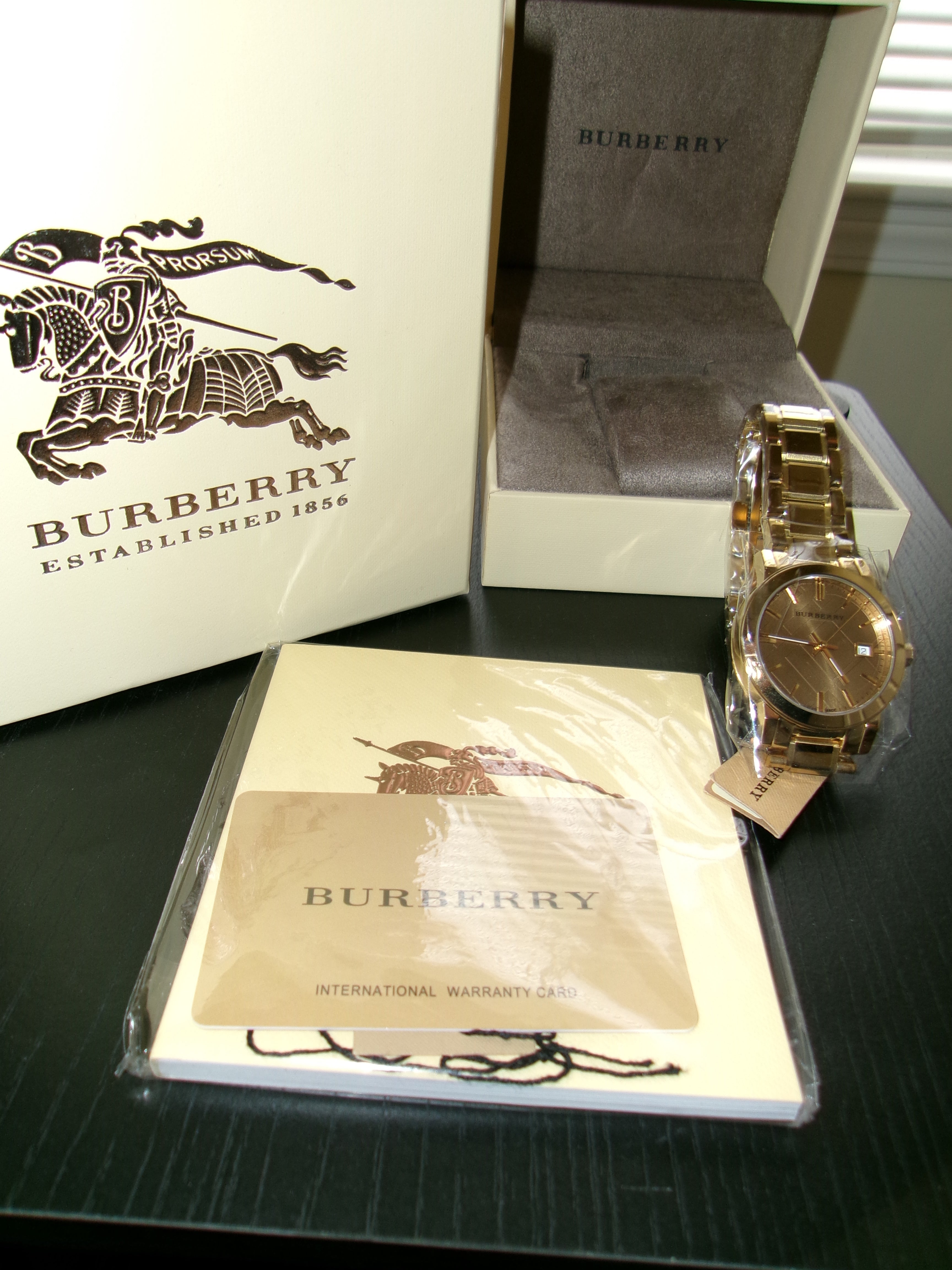 Gold watch on a black surface with Burberry packaging in the background