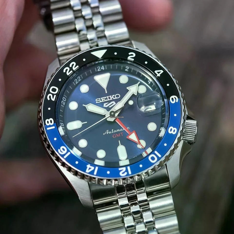Seiko watch with blue bezel and silver metal strap held by a hand.