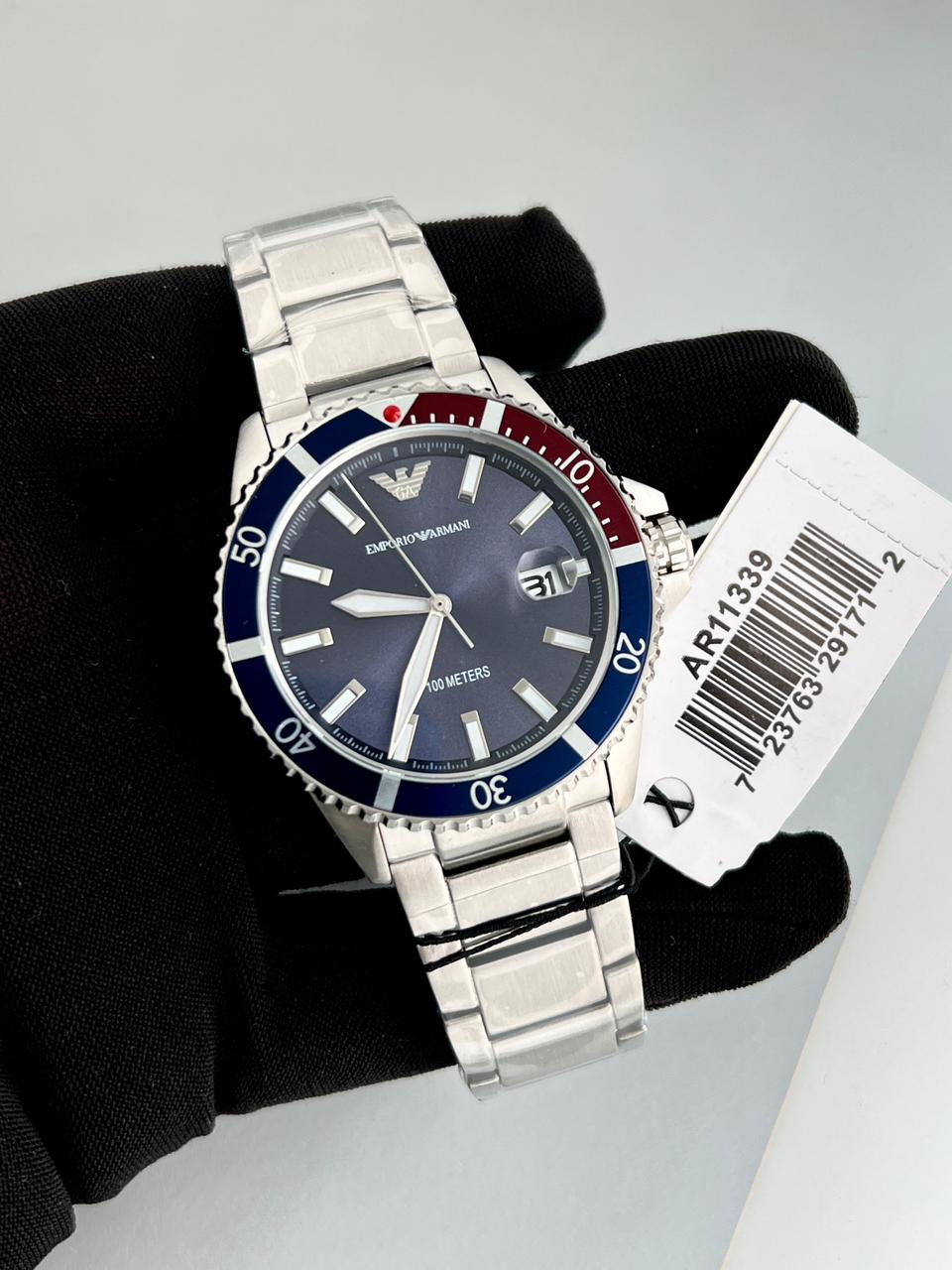 Silver wristwatch with a blue face and red accents on a black cloth background.