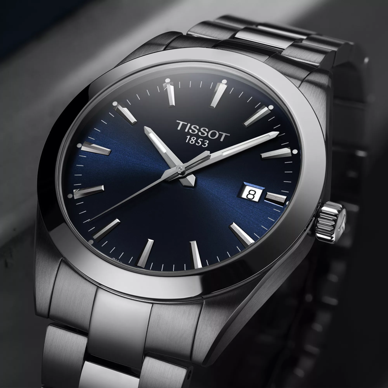 Tissot watch with blue dial and silver metal strap on a dark background