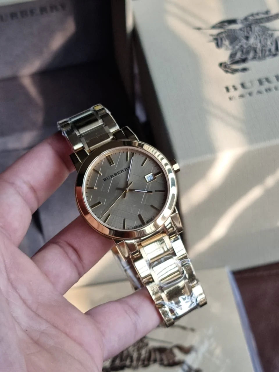 Gold wristwatch held in a hand with a box in the background
