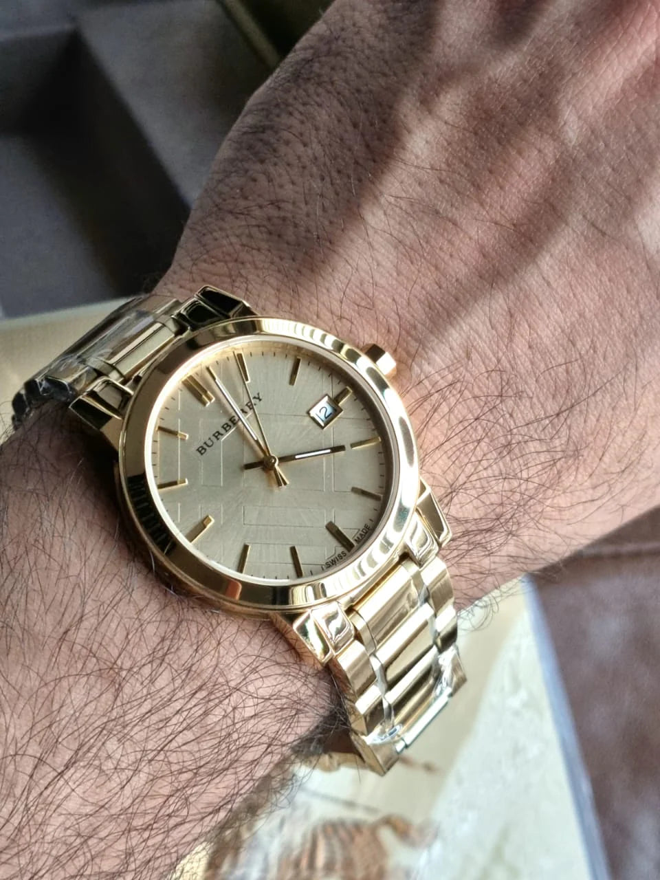 A man's wrist wearing a gold-tone Burberry 'The City' men's watch with a champagne dial and gold-tone bracelet.
